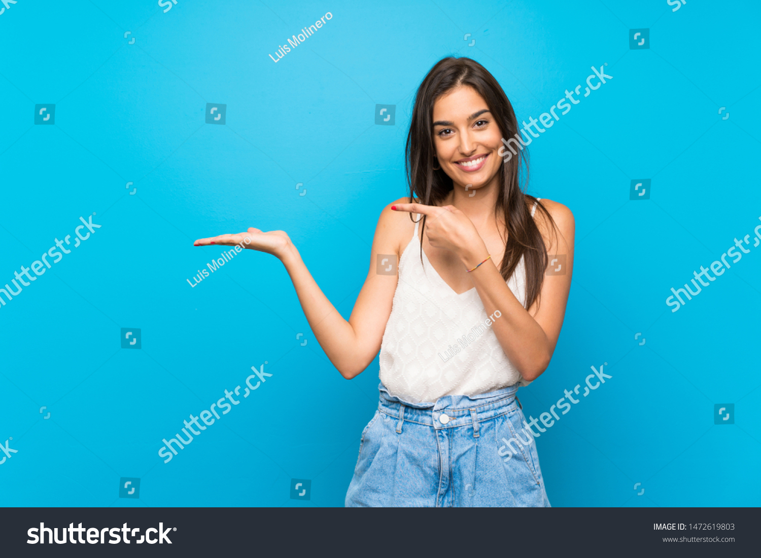 Young woman over isolated blue background holding copyspace imaginary on the palm to insert an ad #1472619803