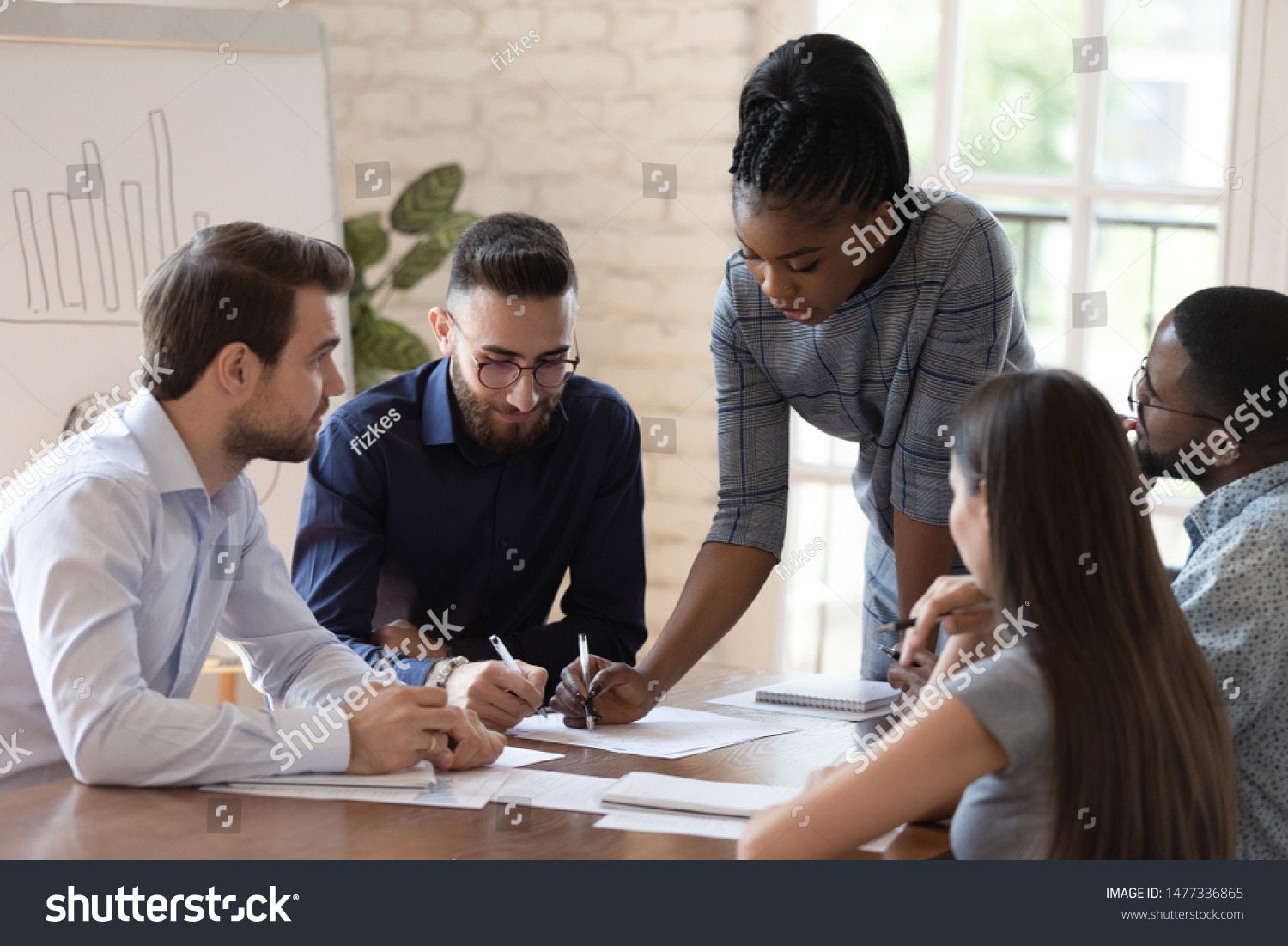 Serious african woman supervisor boss teach diverse staff workers explain project plan paperwork at group meeting, focused black female mentor training business team at corporate office briefing #1477336865