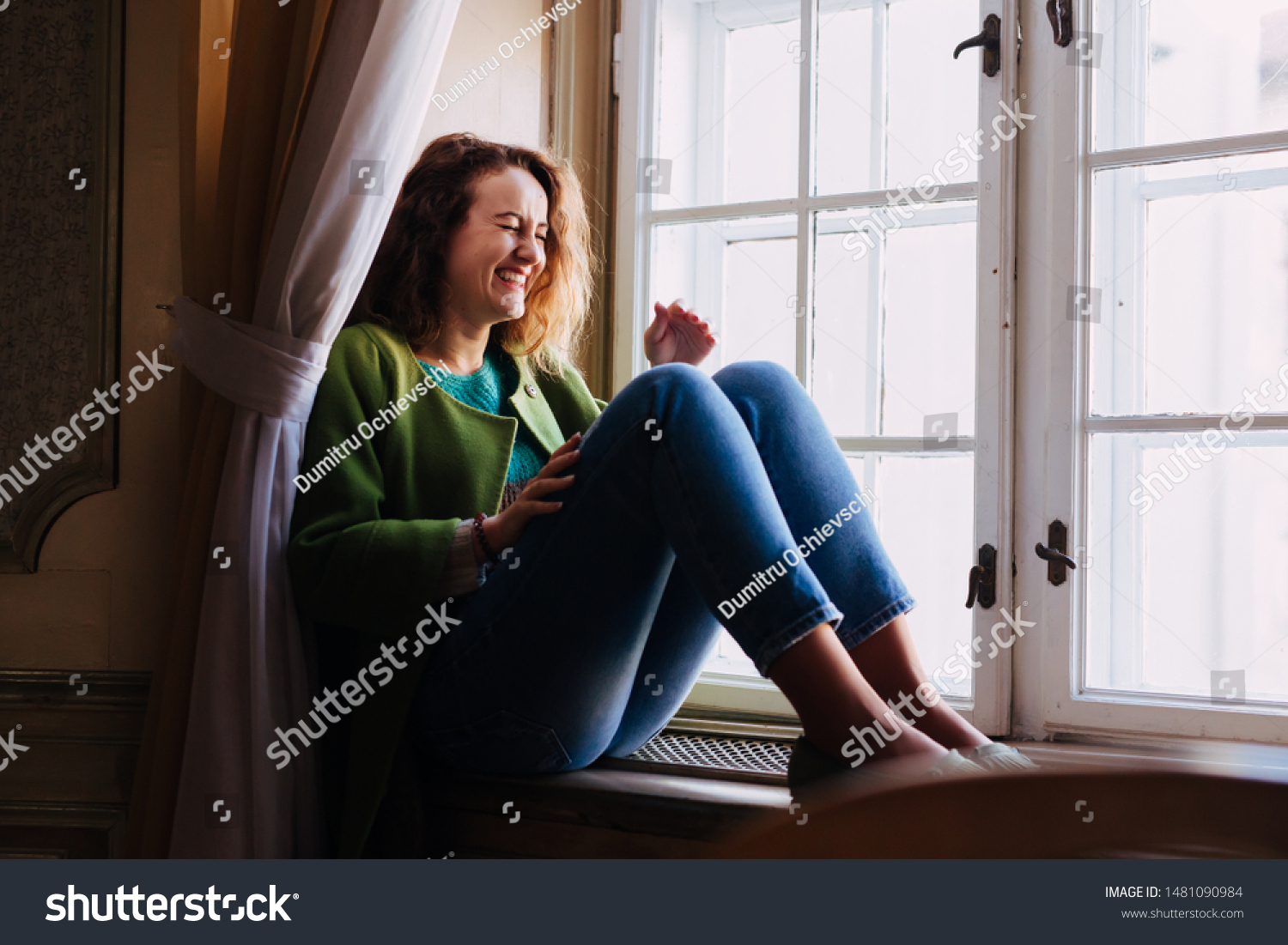 Natural woman laughing spontaneously  near a window. Warm dressed caucasian girl with curly hair. #1481090984