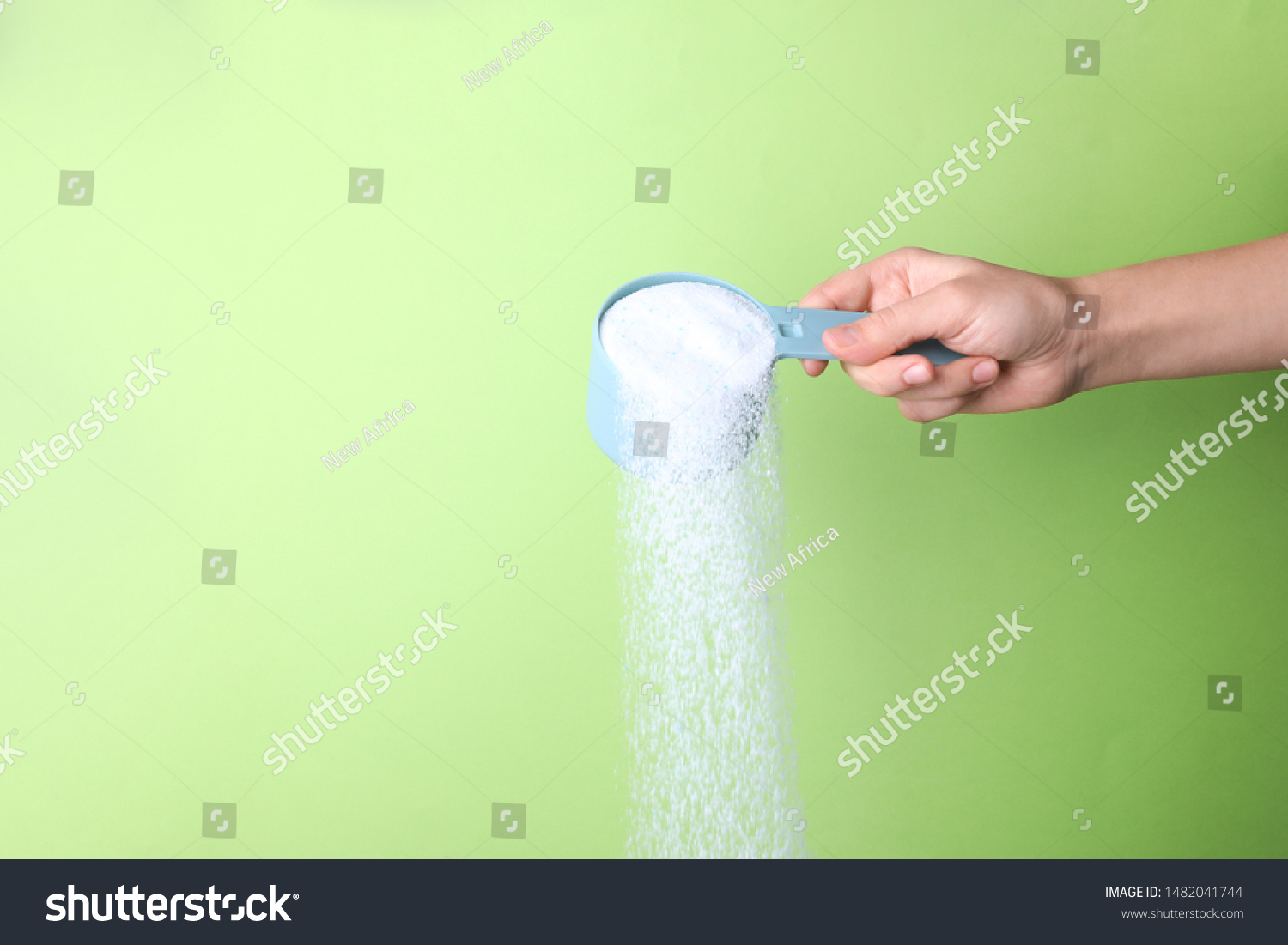 Woman pouring laundry detergent from measuring container against green background, closeup. Space for text #1482041744