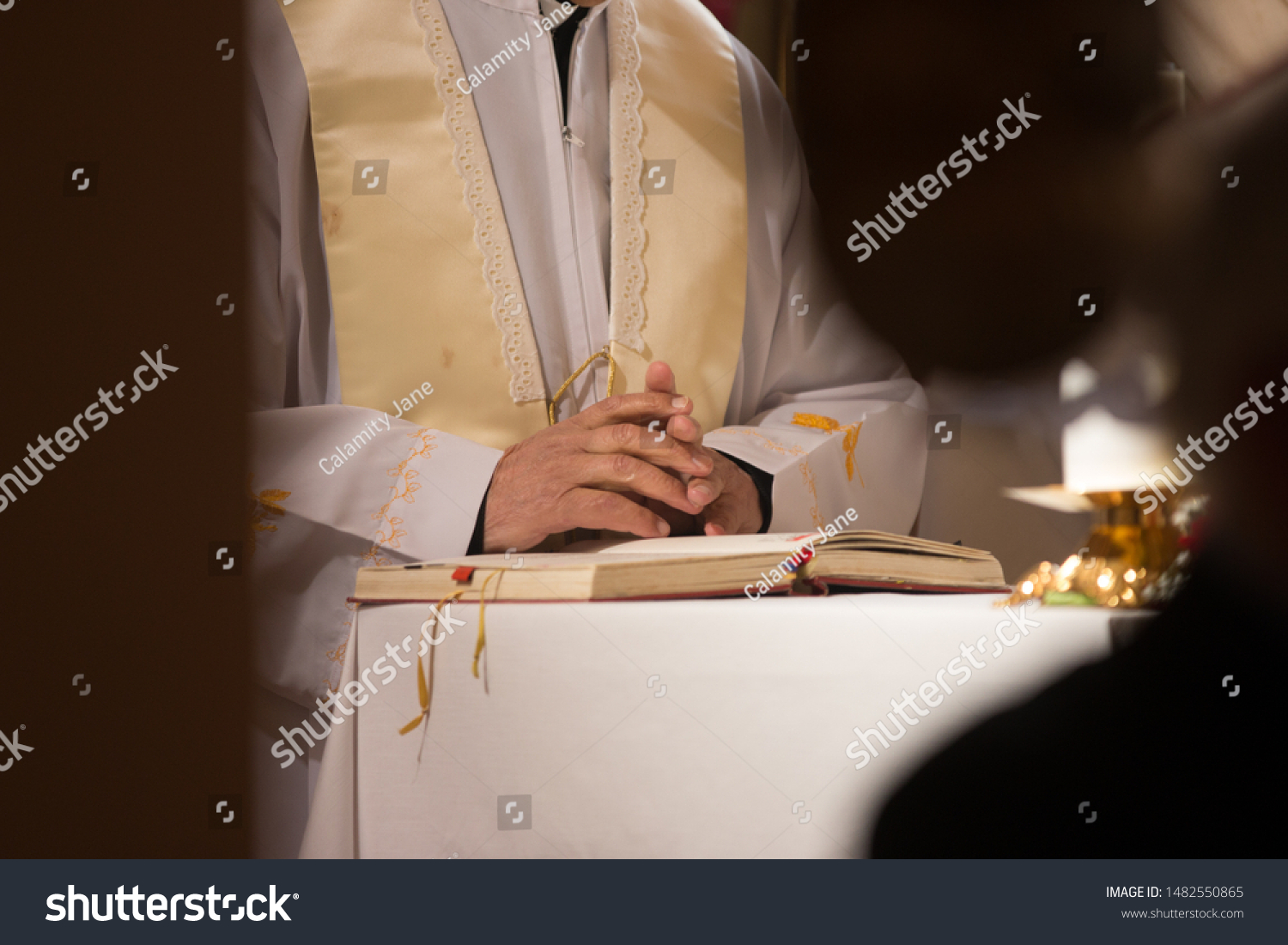 Catholic priest holding hands in prayer above a holy book during mass #1482550865