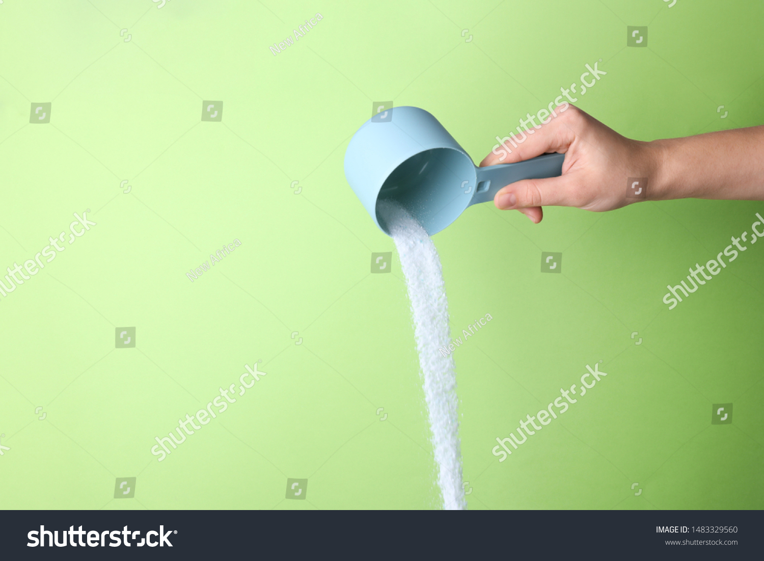 Woman pouring laundry detergent from measuring container against green background, closeup. Space for text #1483329560