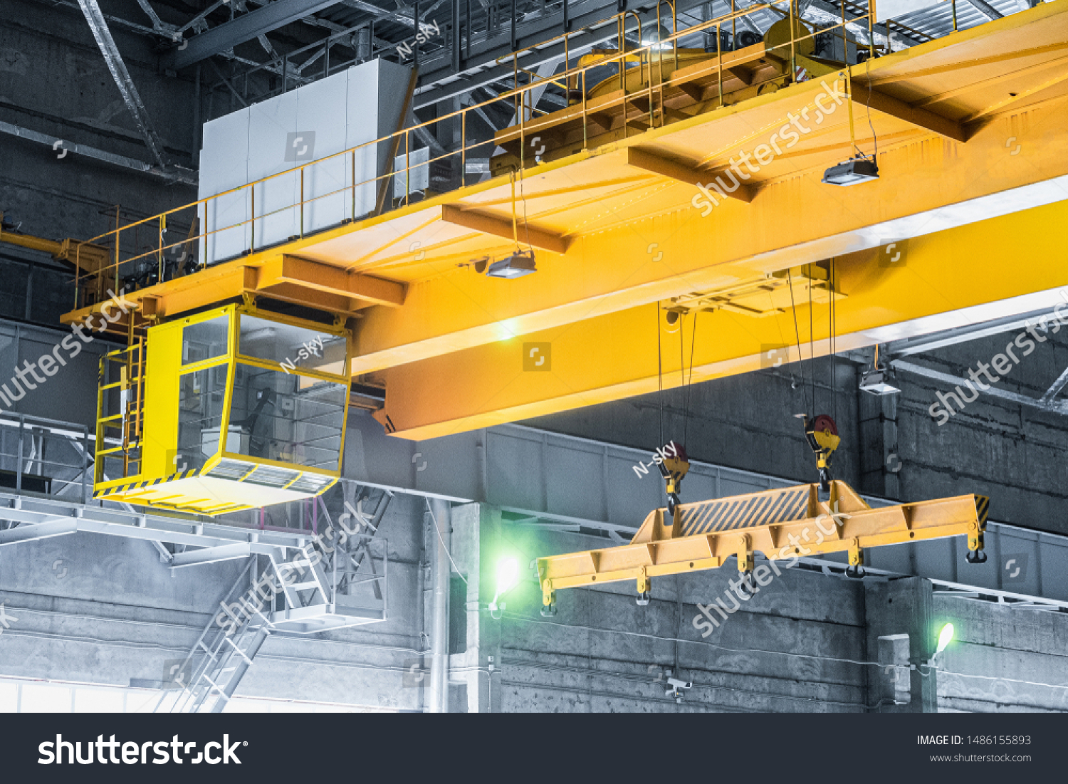 Yellow overhead crane with linear traverse and hooks in engineering plant shop. Cabin of crane operator and jib crab trolley. Landing  staircase. #1486155893