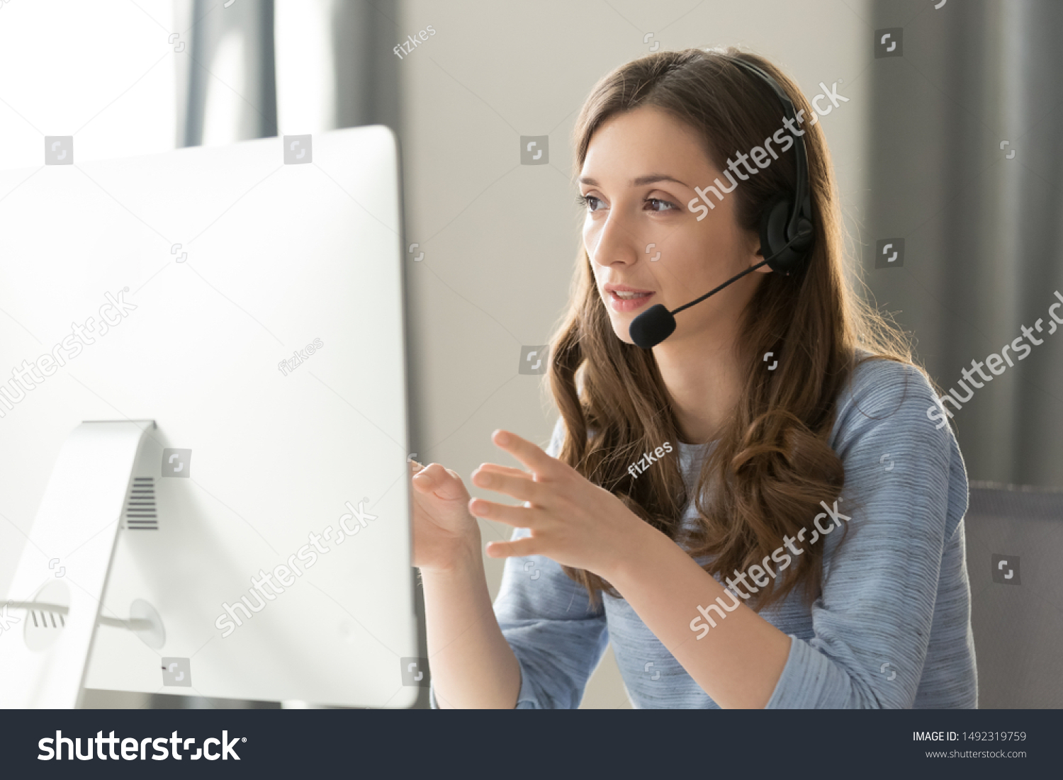 Serious call center operator in wireless headset talking with customer, woman in headphones with microphone consulting client on phone in customer support service, looking at computer screen close up #1492319759
