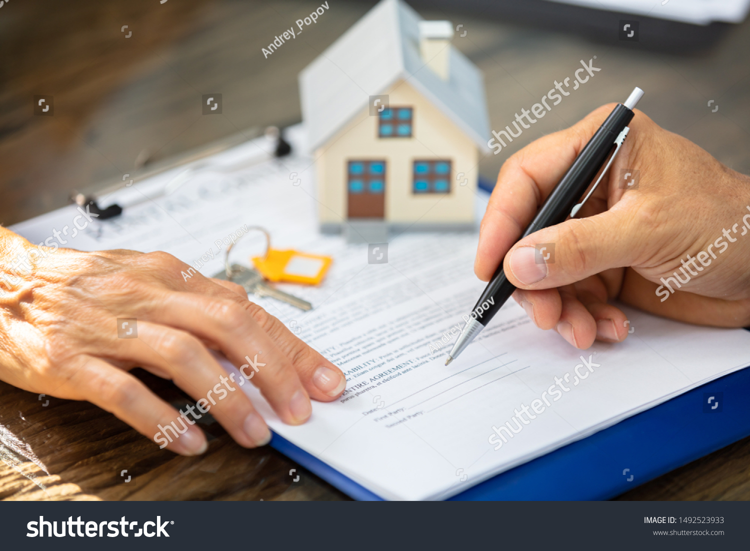Close-up Of A Real Estate Agent's Hand Helping Client In Filling Contract Form Over Desk #1492523933