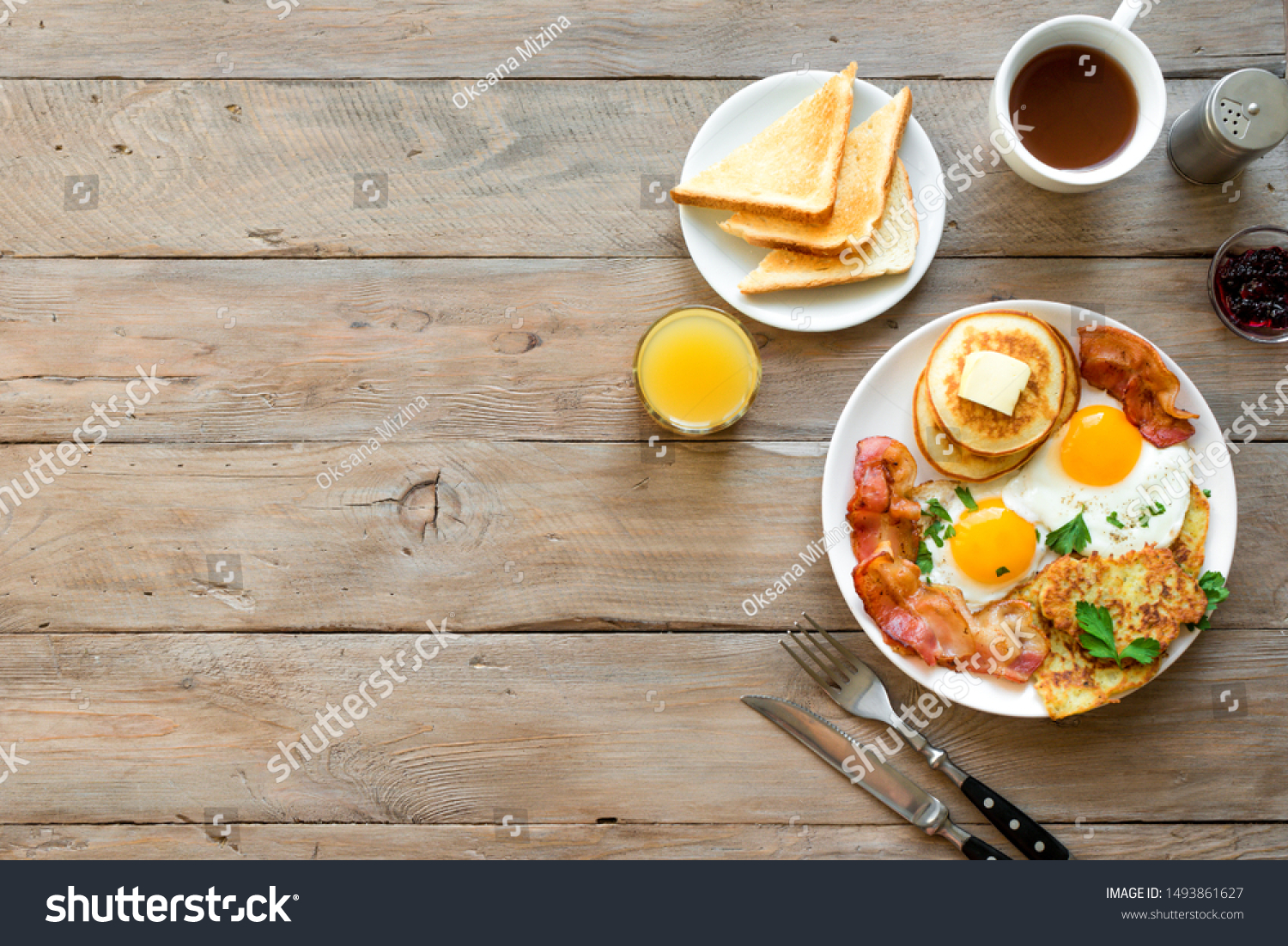Full American Breakfast on wooden, top view, copy space. Sunny side fried eggs, roasted bacon, hash brown, pancakes, orange juice and coffee for breakfast. #1493861627