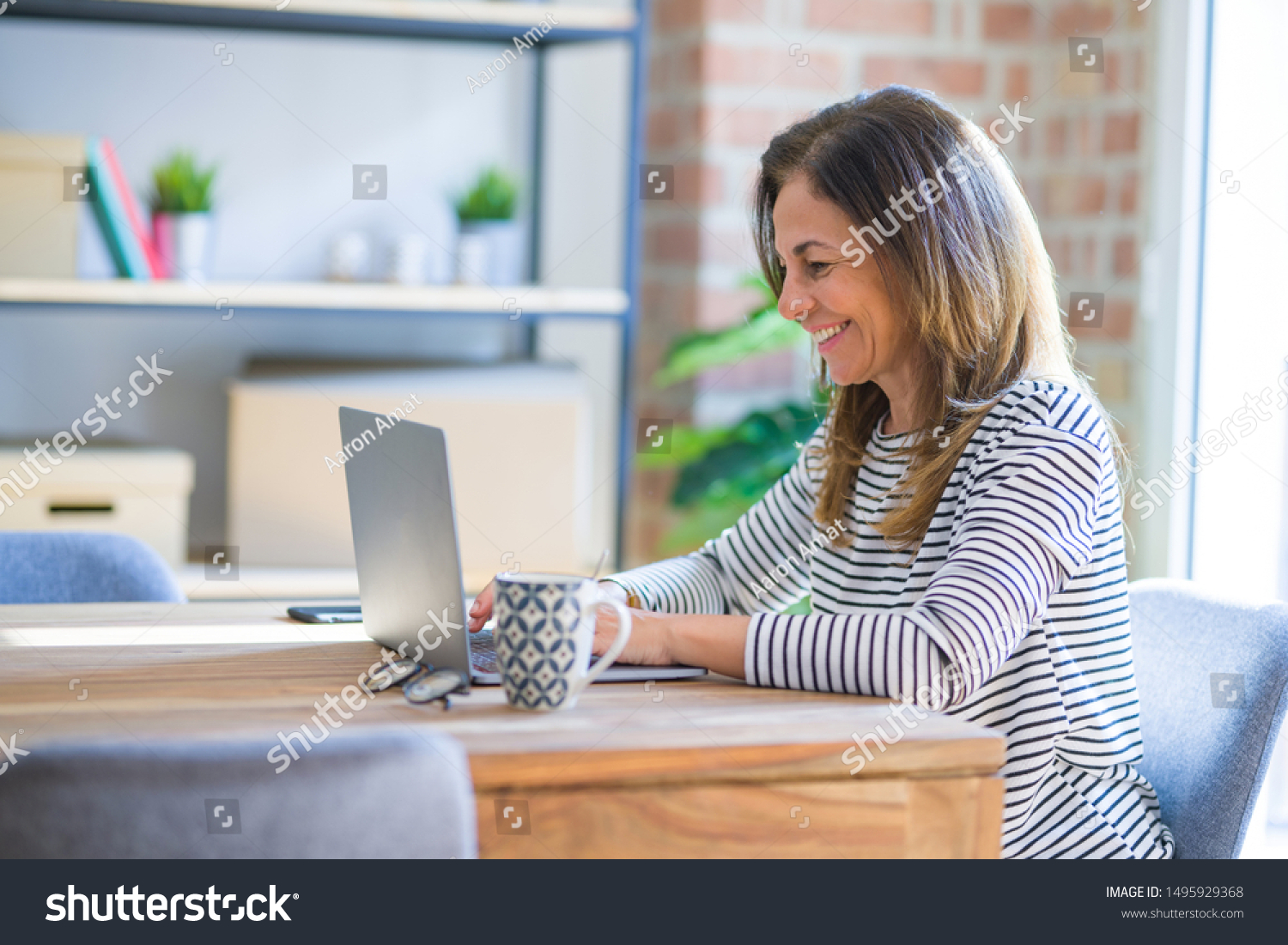 Middle age senior woman sitting at the table at home working using computer laptop with a happy face standing and smiling with a confident smile showing teeth #1495929368
