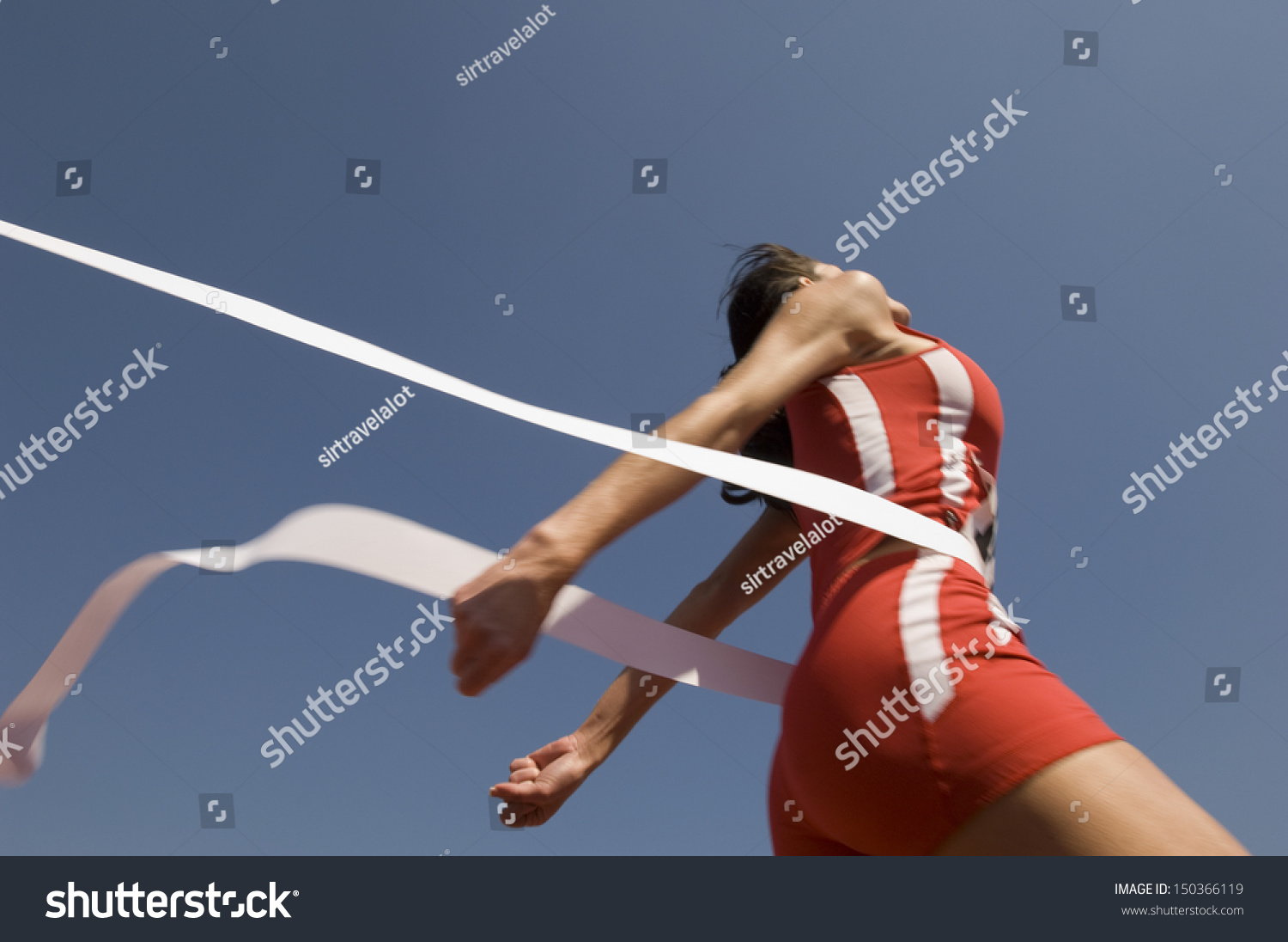 Low angle view of young female athlete crossing finish line against clear blue sky #150366119