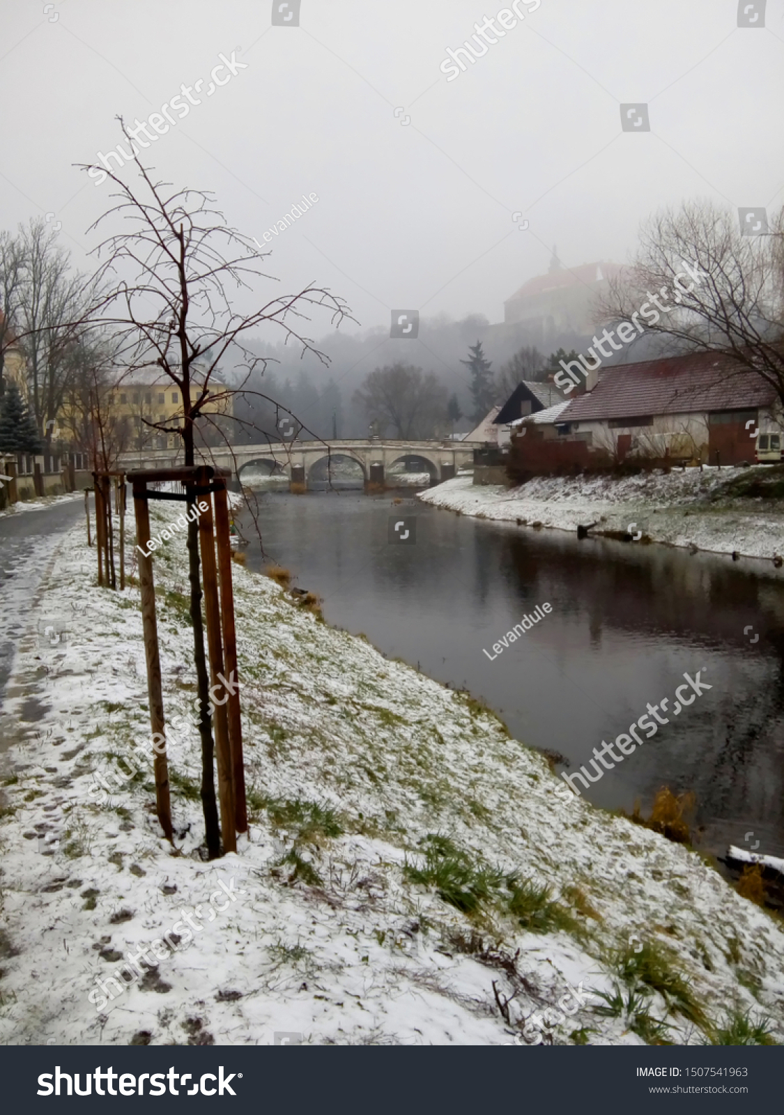 View of the river Oslava in a little historical town Namest nad Oslavou. Czech nature / Czech countryside during  winter time with snow and grey cloudy sky. Moravia, Czech Republic, Central Europe. #1507541963