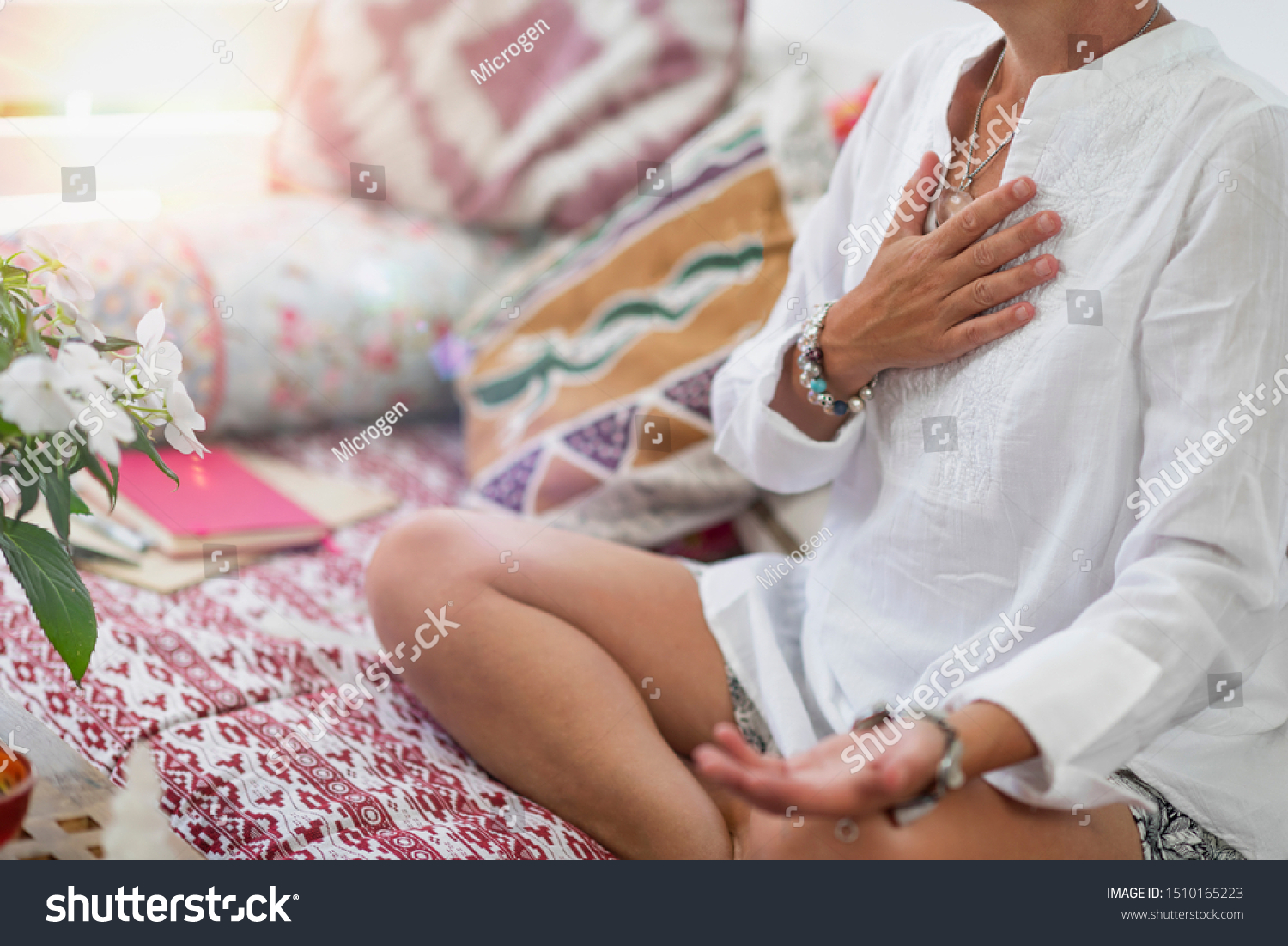 Self-Healing Heart Chakra Meditation. Woman sitting in a lotus position with right hand on heart chakra and left palm open in a receiving gesture. Self-Care Practice at Home #1510165223