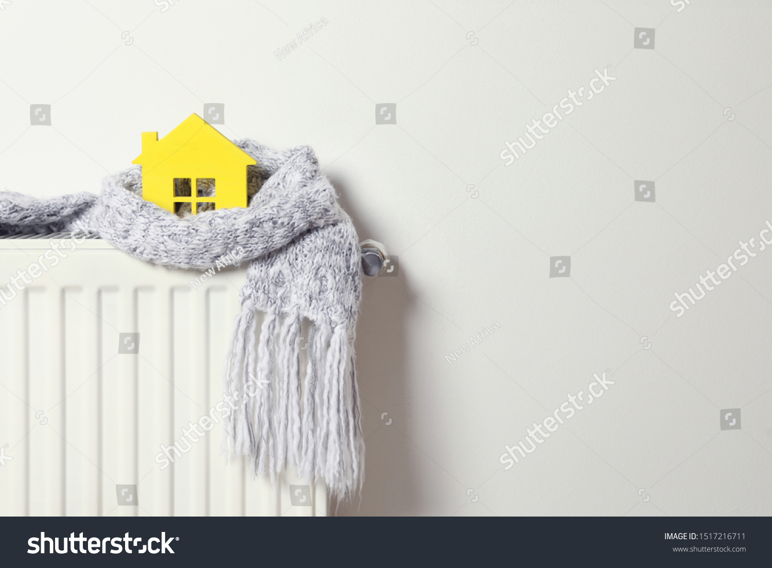 House model wrapped in scarf on radiator indoors, space for text. Winter heating efficiency #1517216711