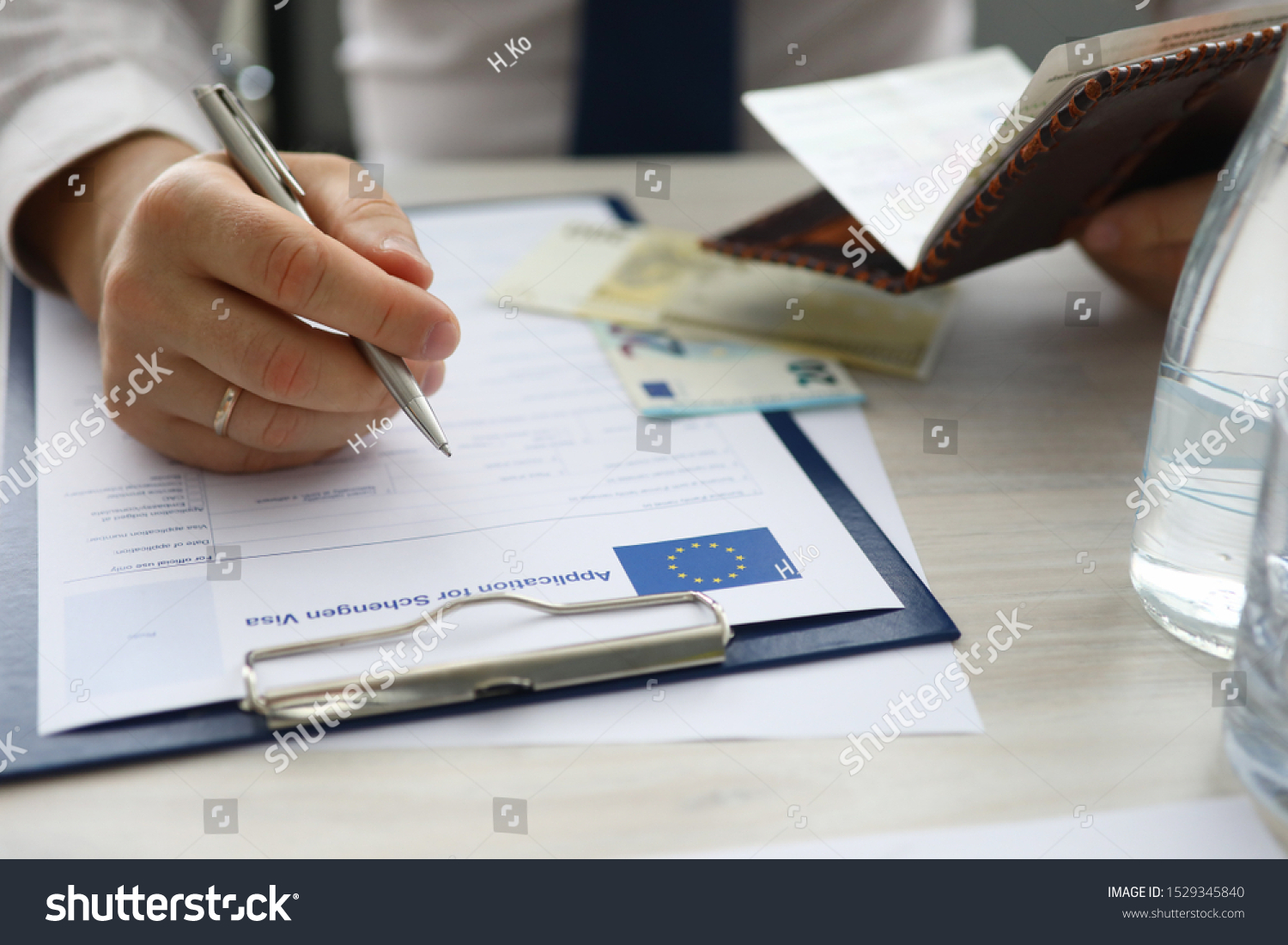 Focus on male hand holding passport and writing personal data in application for schengen visa. Man sitting at office. Travelling abroad or immigration concept. Blurred background #1529345840