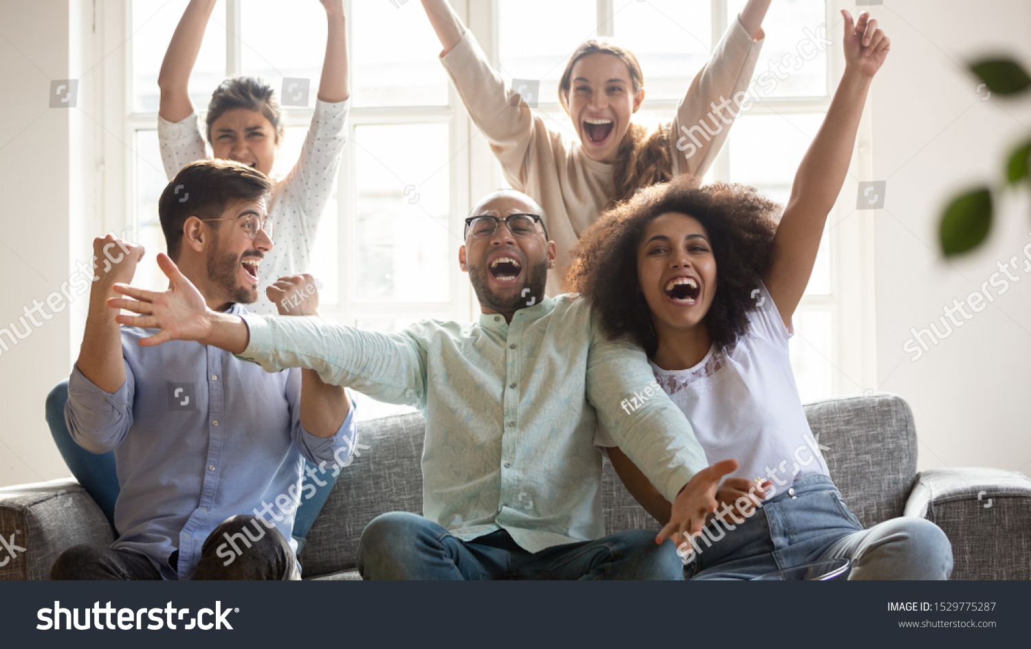 Excited diverse football fans celebrating victory, supporting favorite team, screaming with joy, happy friends watching soccer match on tv together, sitting on couch at home, win sport bet #1529775287