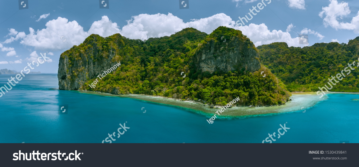 Aerial panoramic drone view of uninhabited tropical island with towering mountains and rainforest jungle surrounded by blue ocean #1530439841