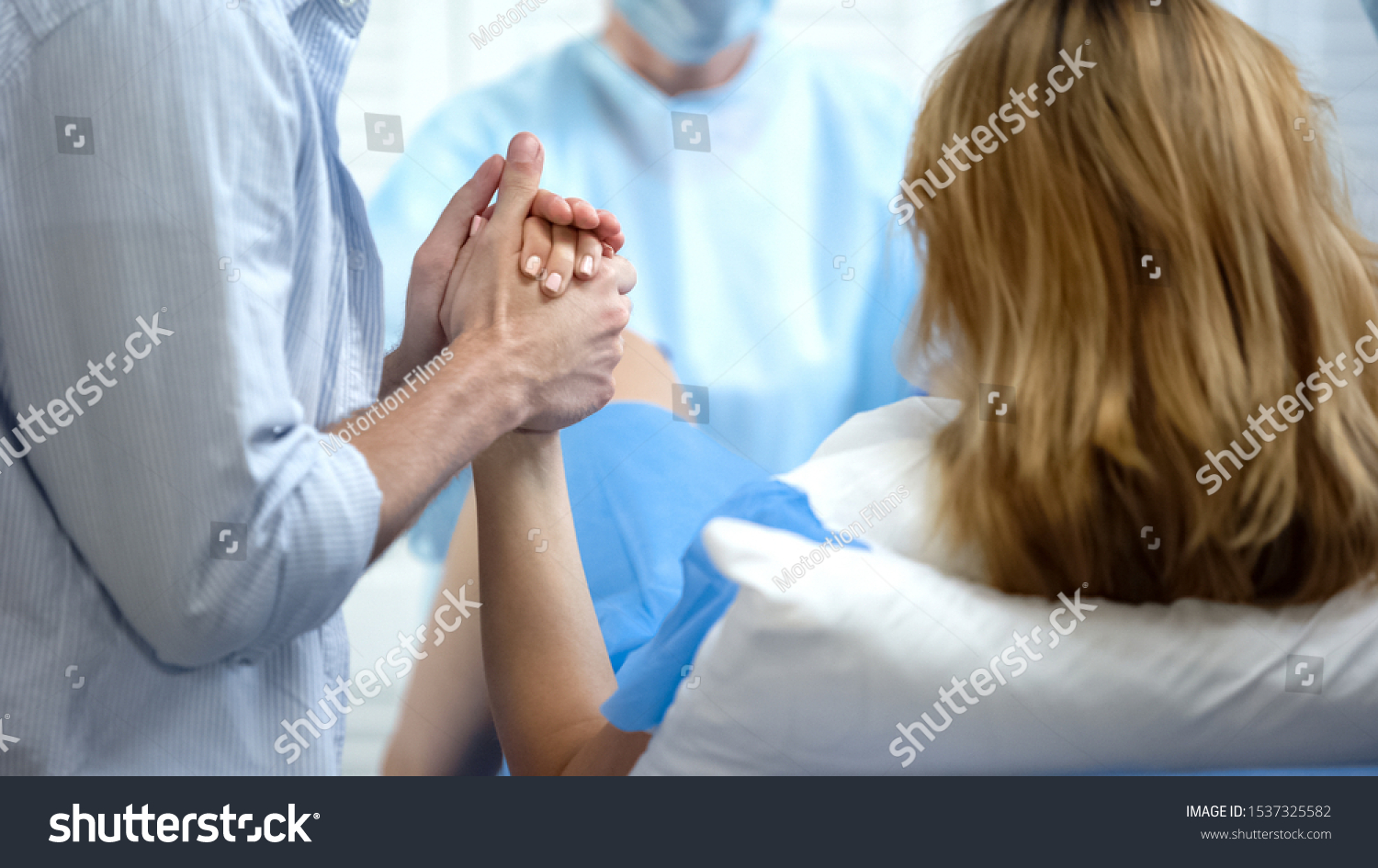 Close-up of man holding wife hand for support during pushing to give childbirth #1537325582