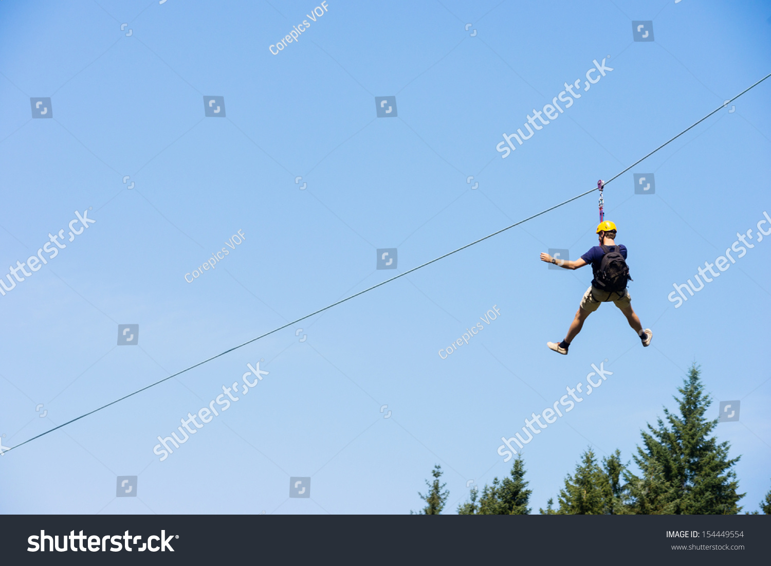 Rear view of young man riding on zip line against blue sky #154449554