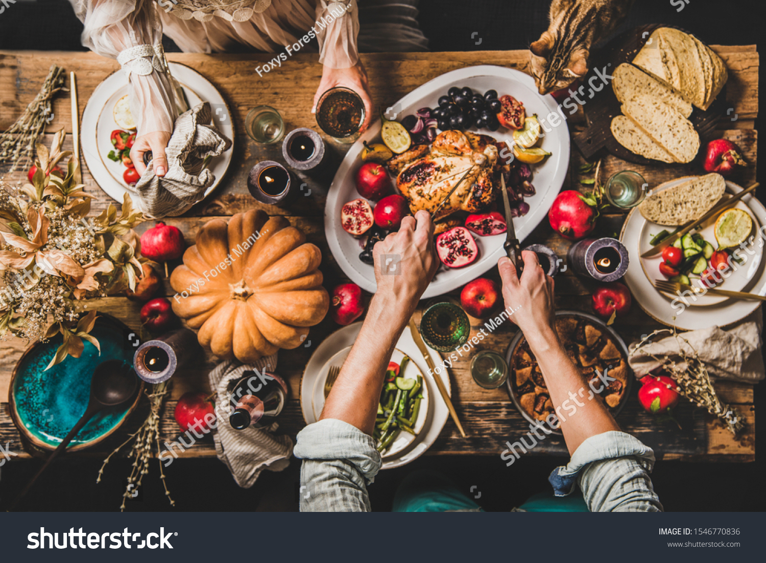 Thanksgiving party table setting. Flat-lay of whole roasted chicken, vegetables, fig pie, fruit, pumpkin, candles, tableware, eating people and tiger cat over rustic wooden table background, top view #1546770836