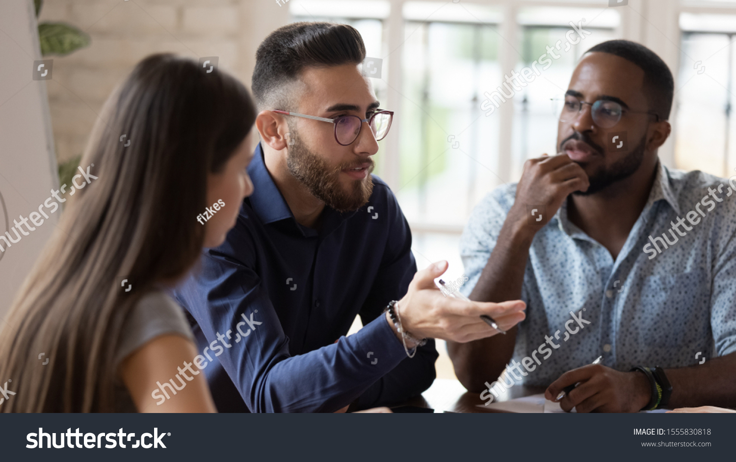 In board room gathered multi racial business people focus on serious middle eastern ethnicity team leader talking about strategy, corporate goals, share ideas, solve problems together at group meeting #1555830818
