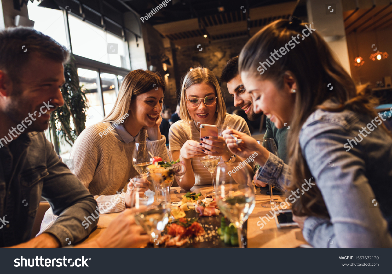Group of young friends having fun in restaurant, talking and laughing while dining at table. #1557632120