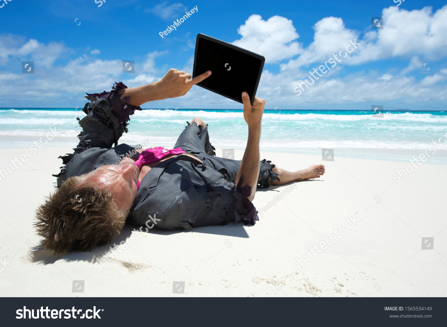 Castaway businessman relaxing with wifi on a tropical beach using his tablet computer #1565534149