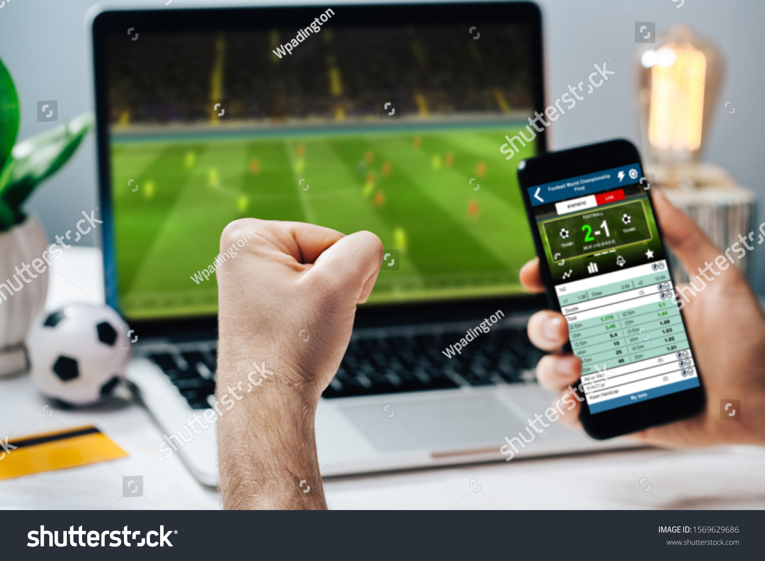Lucky man celebrating money win. Male fan watching football play online broadcast on his laptop, cheering for his favorite team and making bets at bookmaker's website. #1569629686