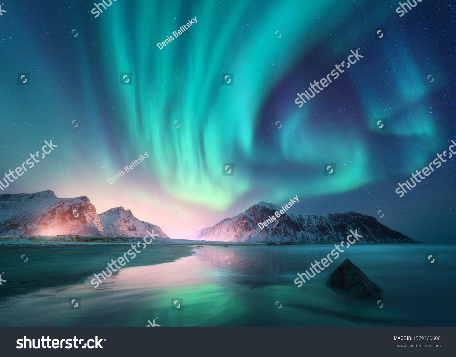 Aurora borealis over the sea, snowy mountains and city lights at night. Northern lights in Lofoten islands, Norway. Starry sky with polar lights. Winter landscape with aurora, reflection, sandy beach  #1579360606