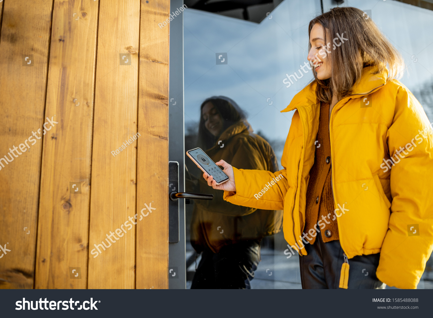 Woman locking smartlock on the entrance door using a smart phone. Concept of using smart electronic locks with keyless access #1585488088