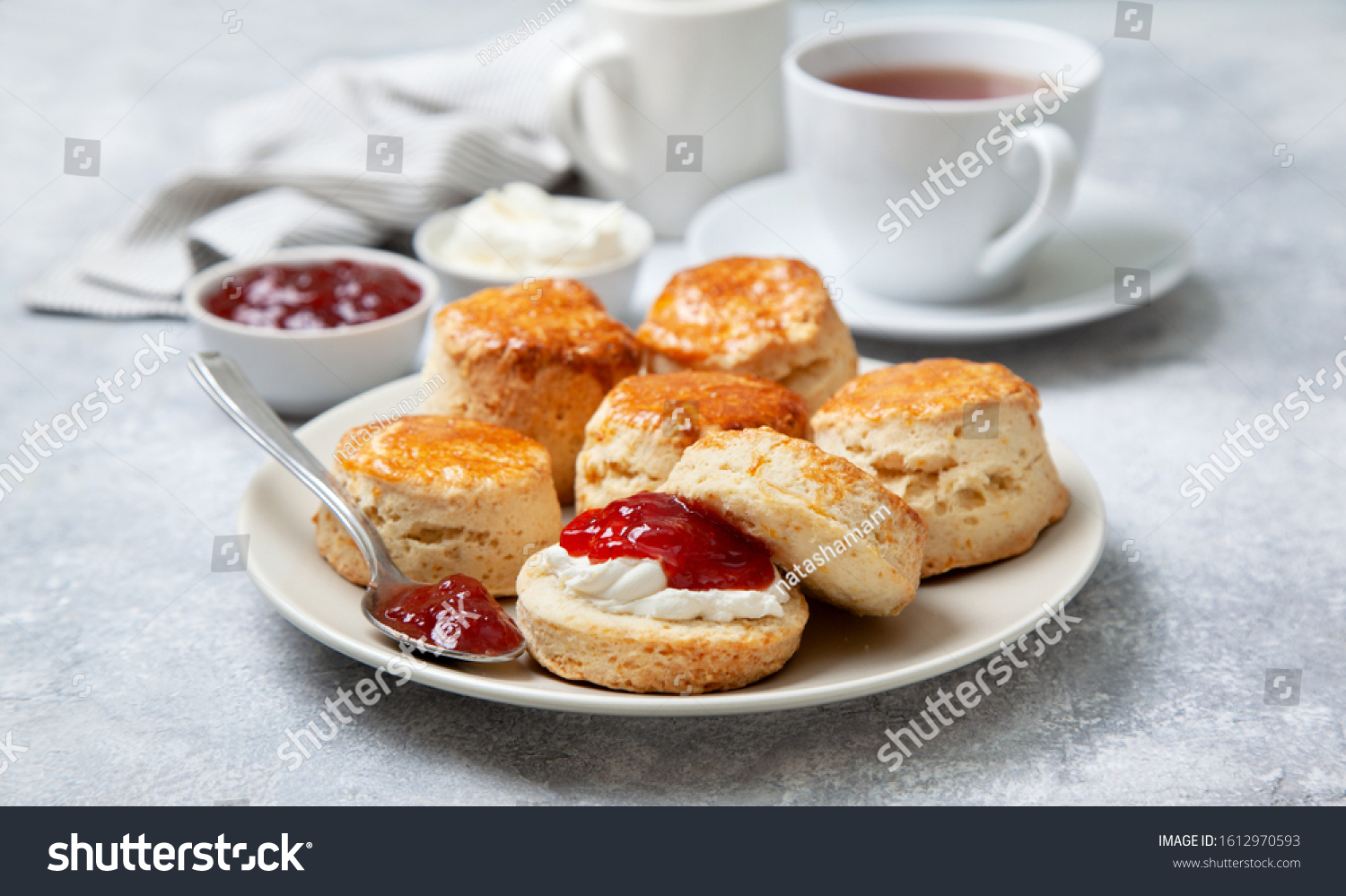 scones on a white plate, a jar of strawberry jam and a cup of tea on a gray background #1612970593