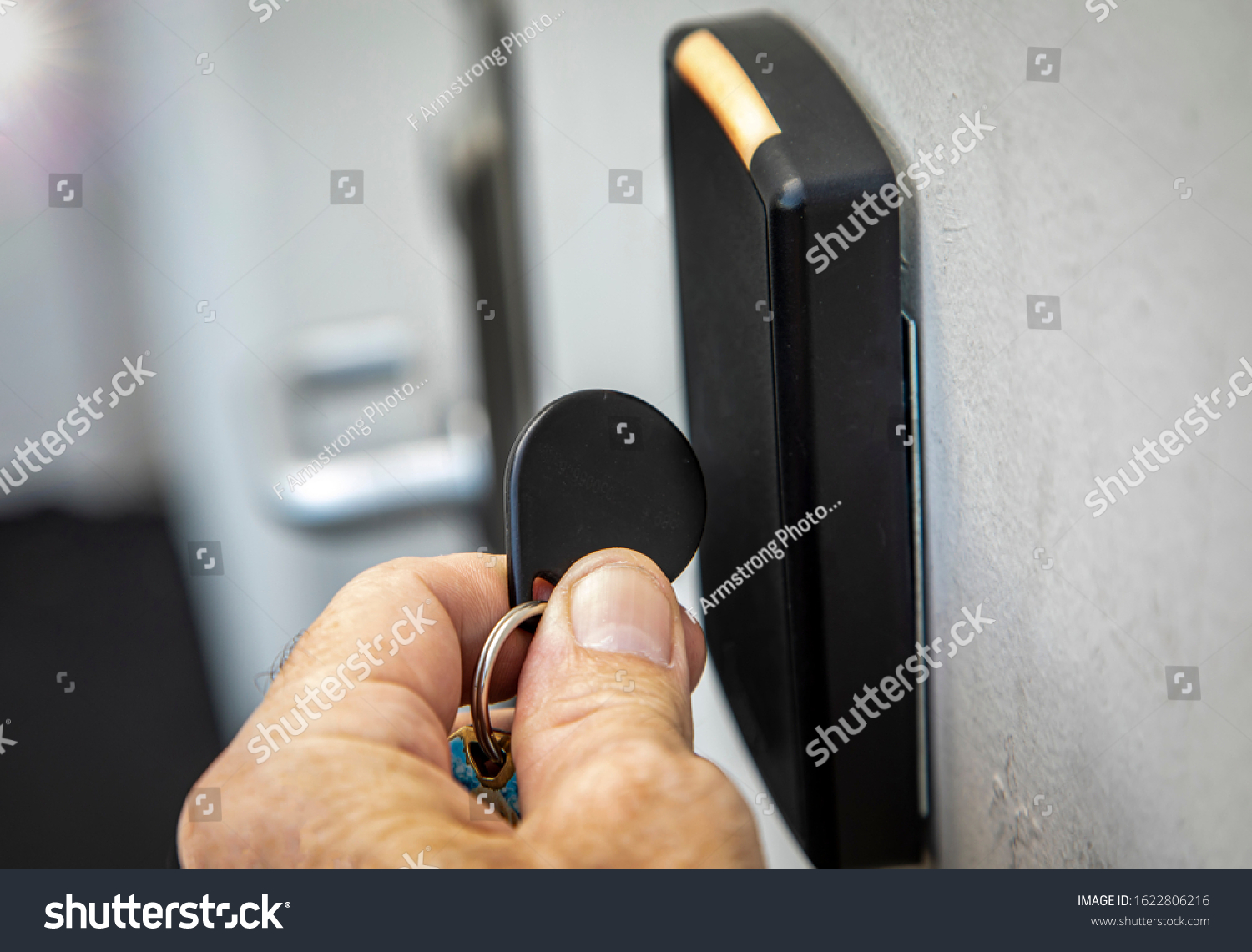 Fingers holding key fob on key fob sensor with door handle out of focus in the distance.  #1622806216