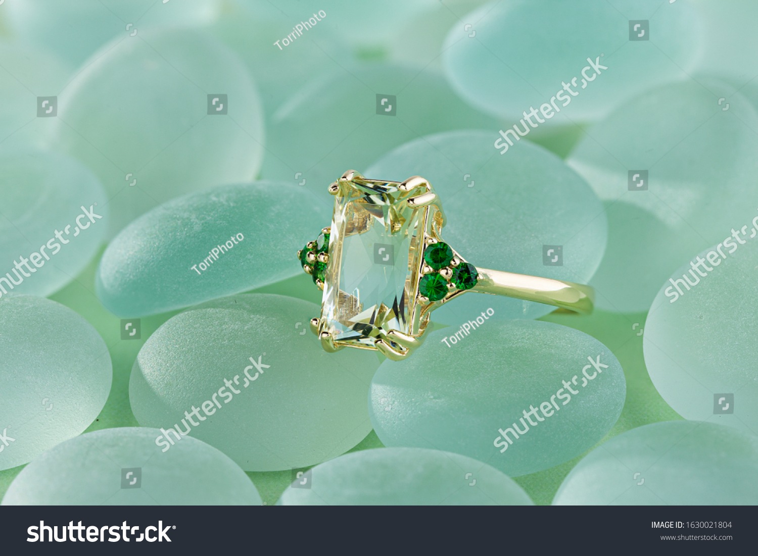 Elegance gold ring with beryl gem and emerald on pastel blue backround. Fashion gold jewelry with gemstone #1630021804