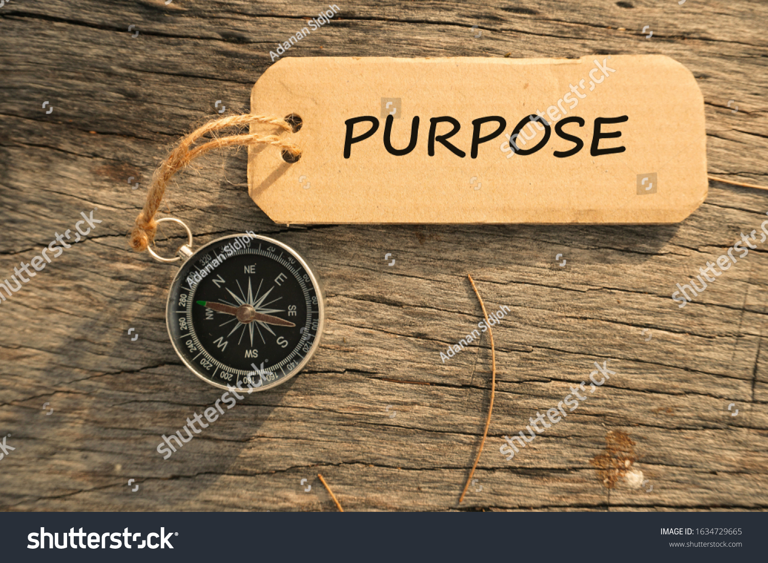 Magnetic compass and text PURPOSE written on paper tag at outdoor. Conceptual image with selective focus #1634729665