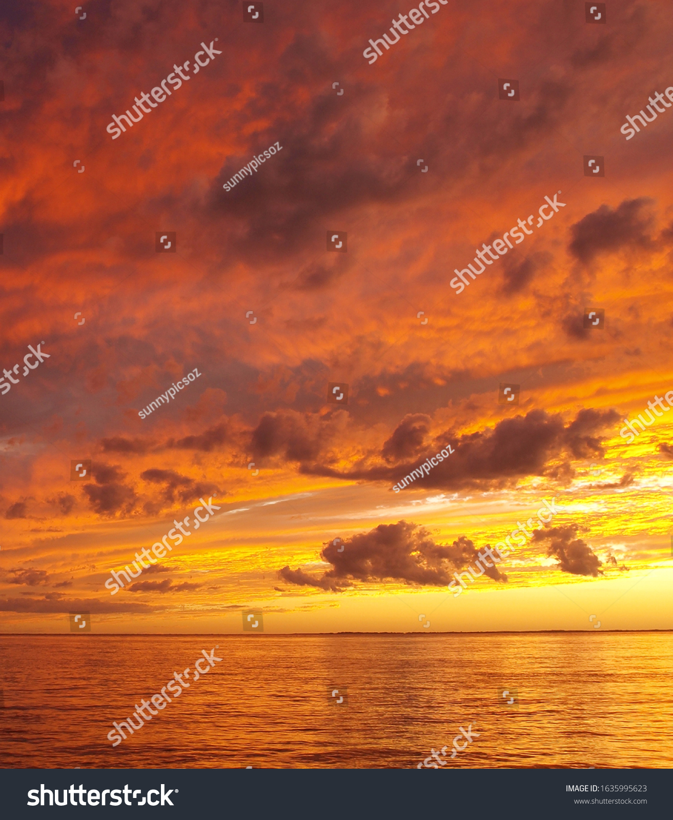 A sunny inspirational orange coloured stratocumulus cloudy coastal sunset seascape over the ocean with water reflections. Queensland, Australia. #1635995623