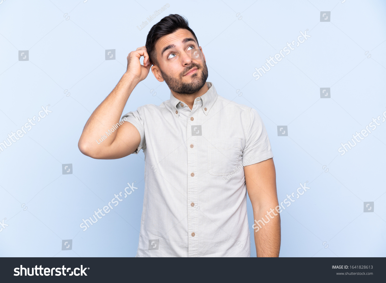 Young handsome man with beard over isolated blue background having doubts and with confuse face expression #1641828613