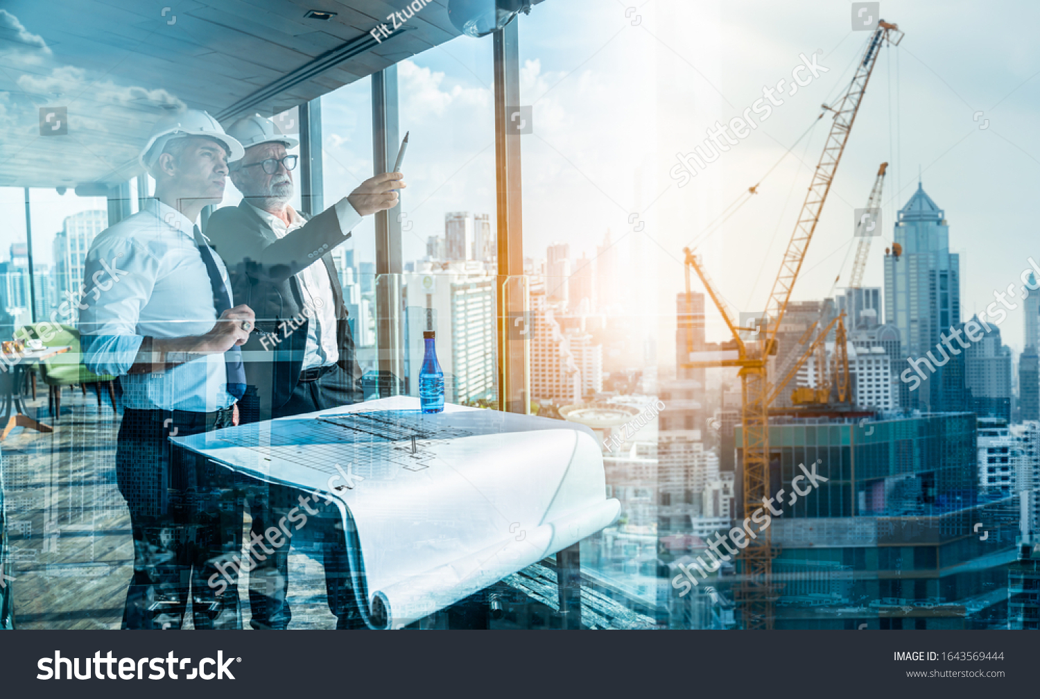 Two Engineer or Architect are analyzing blueprints while working on a new project on construction site with blue sky and city background.Architect supervising construction on terrace tower. #1643569444