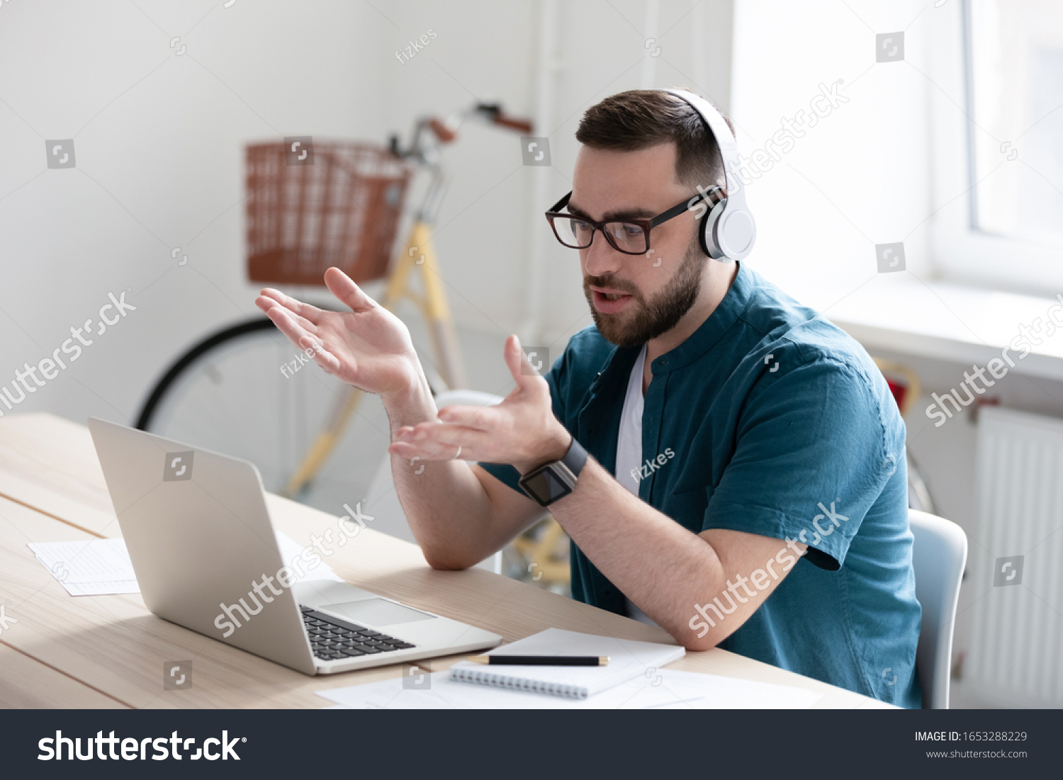 Focused young businessman in eyewear wearing headphones, holding video call with clients on laptop. Concentrated millennial man in glasses giving online educational class lecture, consulting customer. #1653288229