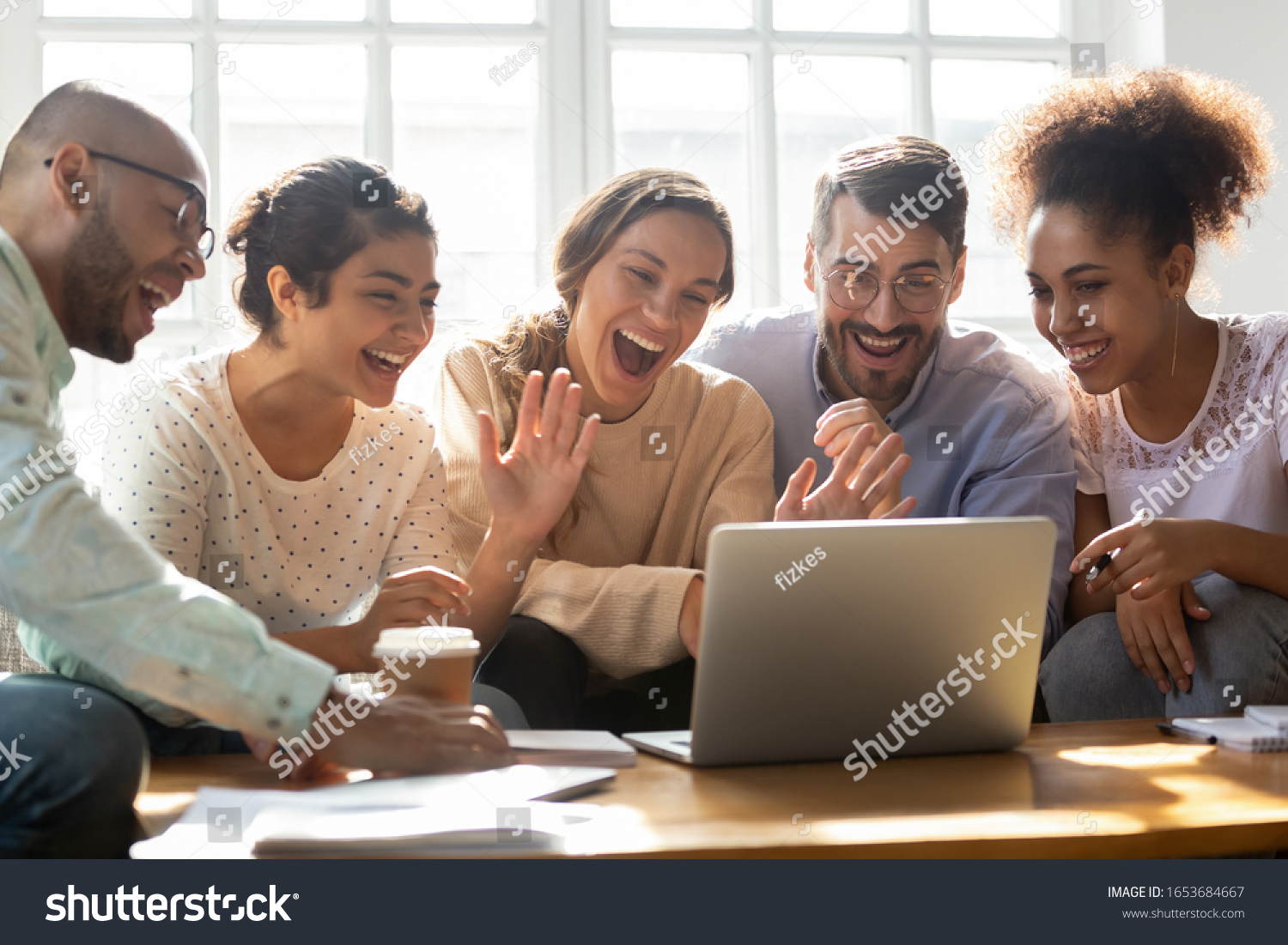 Five multi-ethnic millennial friends sitting on sofa looking at computer screen wave hands laughing enjoy distant communication with mate. Make videocall, greeting online by webcam modern tech concept #1653684667