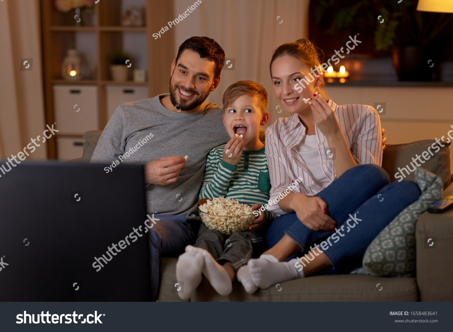 family, leisure and people concept - happy smiling father, mother and little son eating popcorn and watching tv at home in evening #1658483641