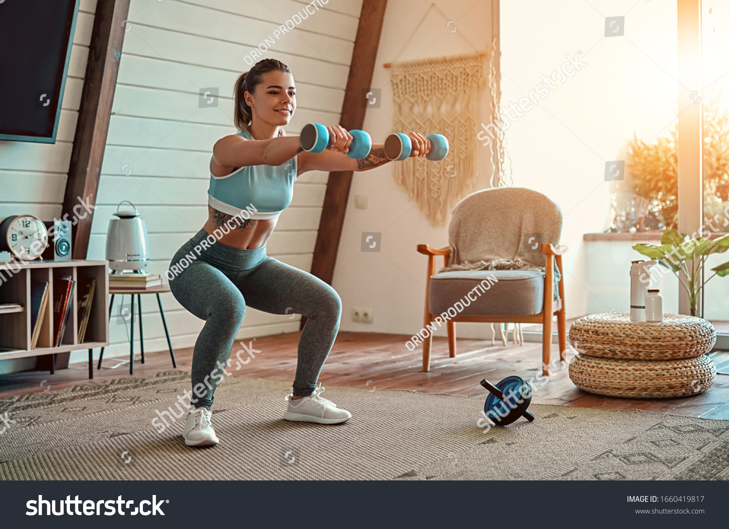 Beautiful young athletic girl in leggings and top crouches with dumbbells at home. Sport, healthy lifestyle. #1660419817
