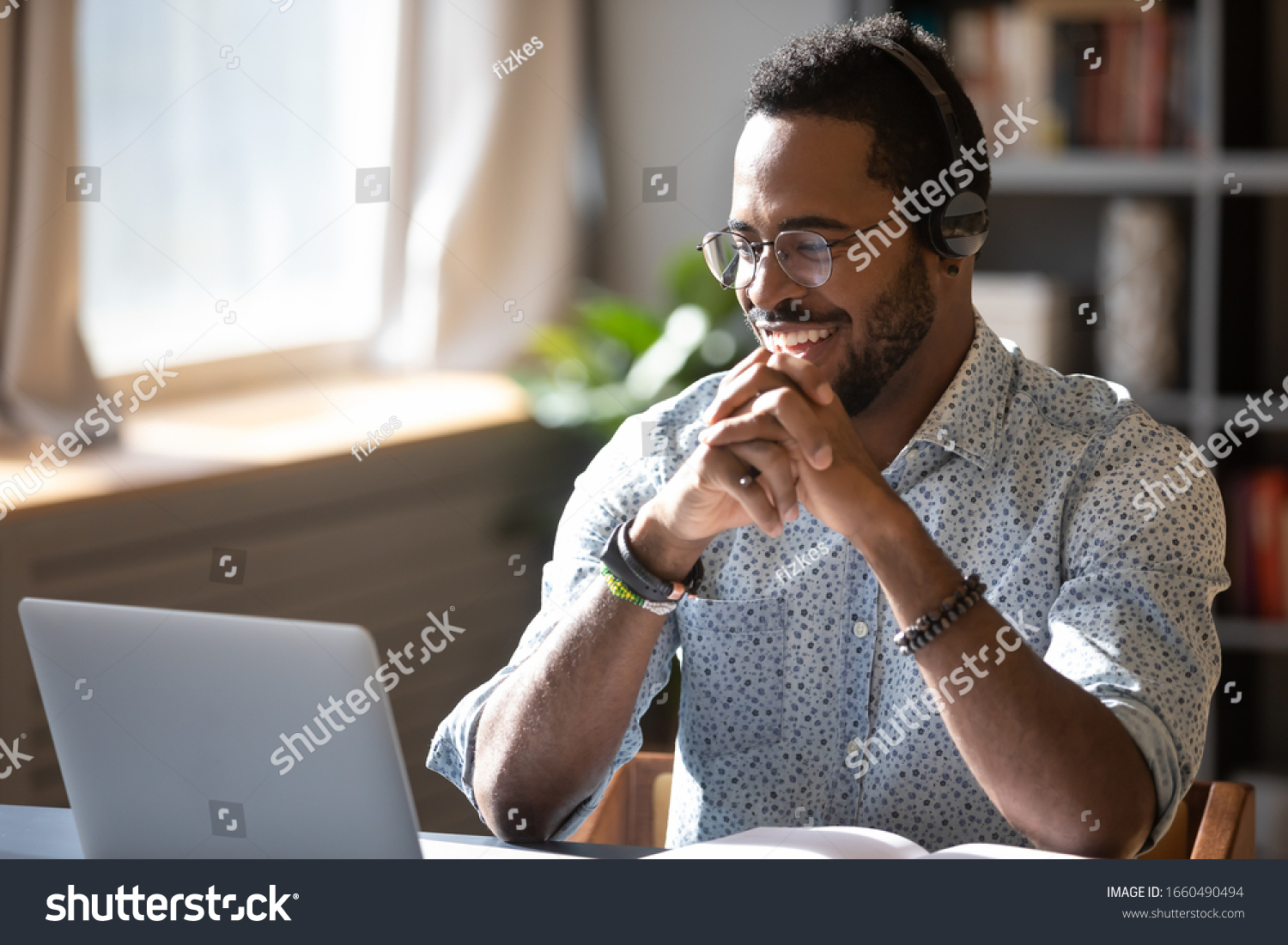 Happy millennial african american man in glasses wearing headphones, enjoying watching educational webinar on laptop. Smiling young mixed race businessman holding video call with clients partners. #1660490494