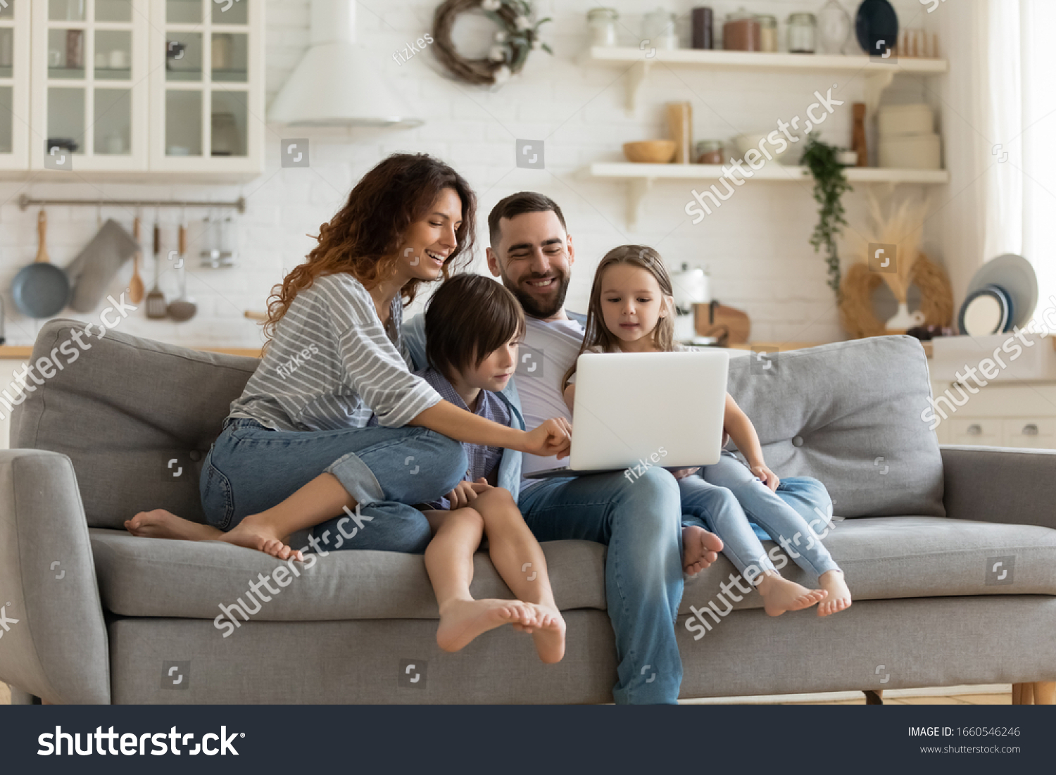 Happy young family with little kids sit on sofa in kitchen have fun using modern laptop together, smiling parents rest on couch enjoy weekend with small children laugh watch video on computer at home #1660546246