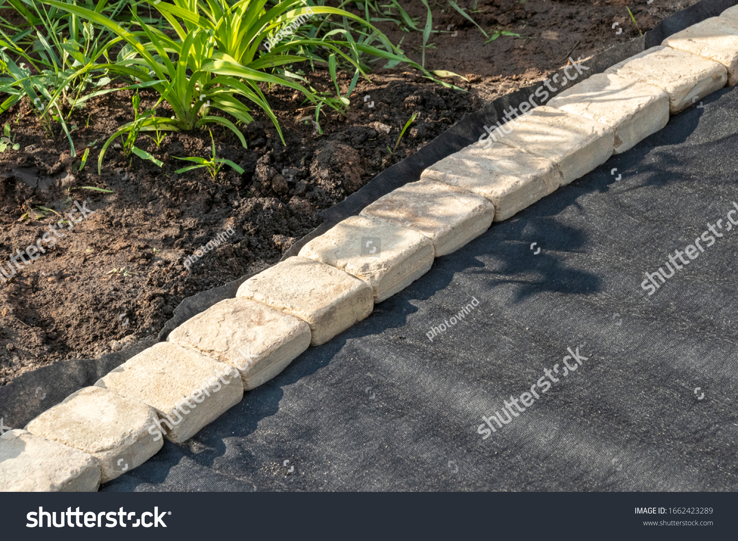 Edging of laid woven geotextile fabric with sandstone pavers in the summer garden under reconstruction #1662423289