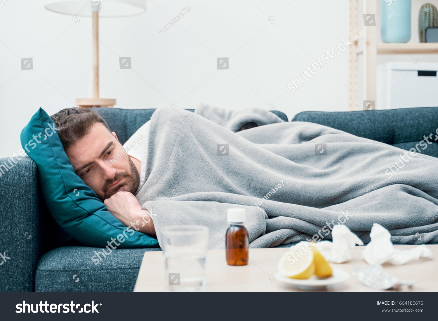 Man wrapped in plaid lying on the sofa feeling sick illness at home #1664185675