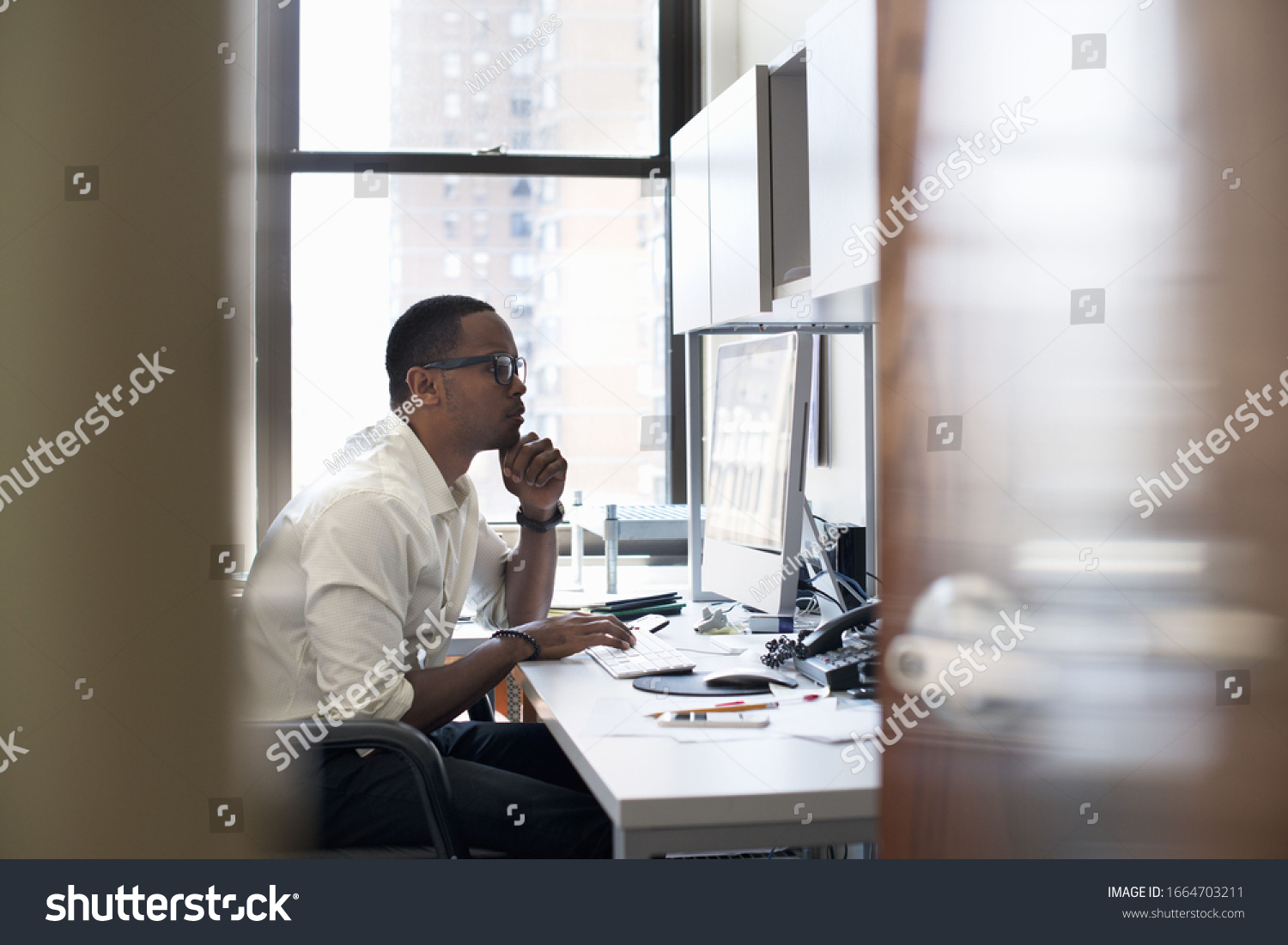 A man working in an office seated at a desk. Looking at a computer screen. #1664703211