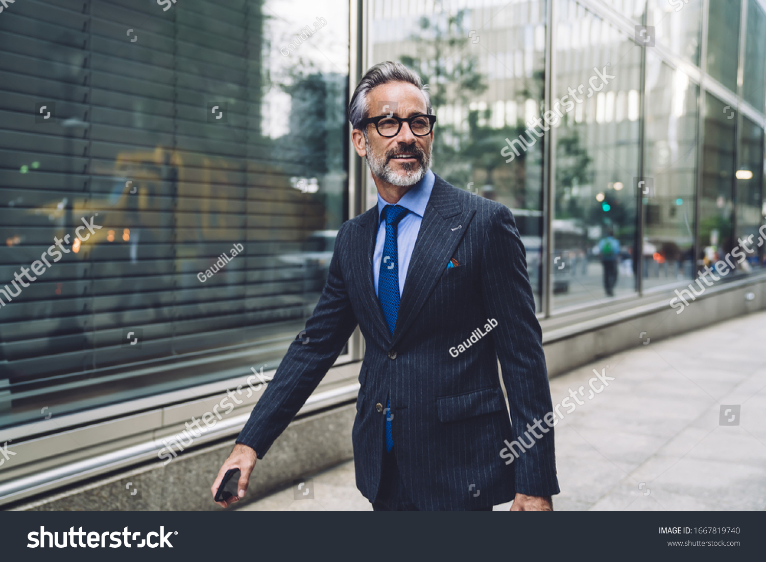 Successful elegant middle aged male executive in expensive suit walking purposefully on New York City street and turning head to side #1667819740