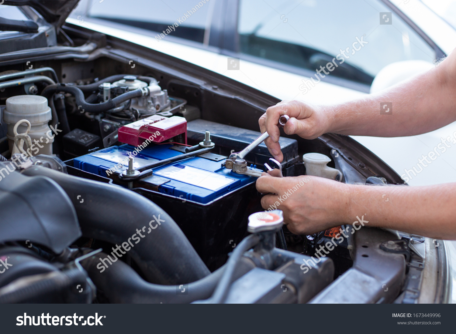 a man tightens with a wrench bolts for fastening a new battery, installing spare parts for a car #1673449996