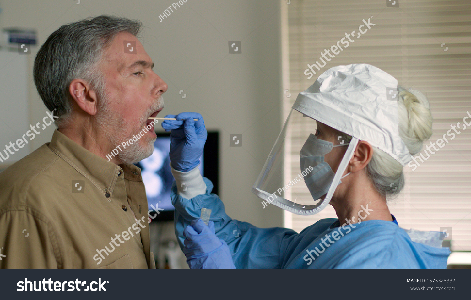 A mature Caucasian man in a clinical setting being swabbed by a healthcare worker in protective garb to determine if he has contracted the coronavirus or COVID-19. #1675328332