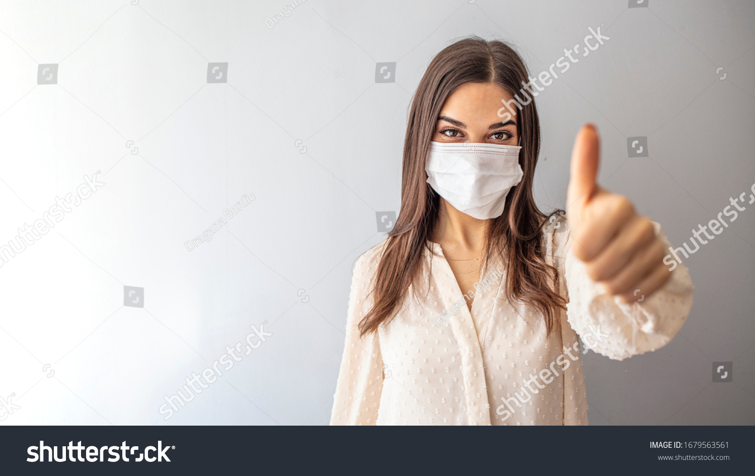 Beautiful caucasian young woman with disposable face mask. Protection versus viruses and infection. Studio portrait, concept with white background. Woman showing thumb up.  #1679563561