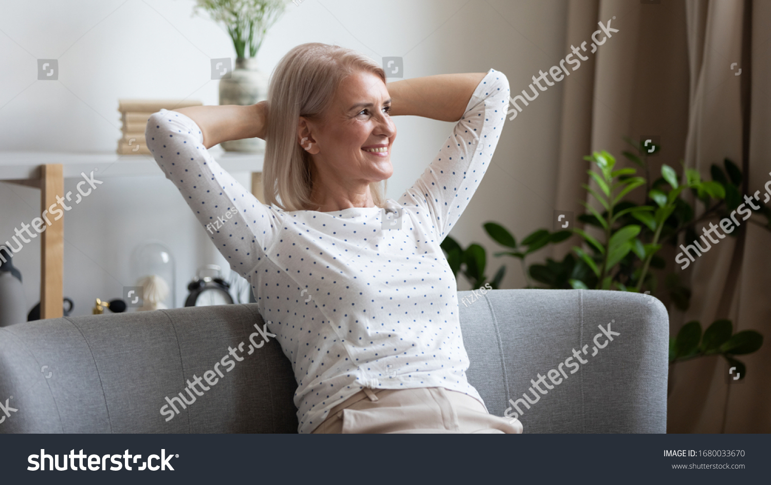 Pleasant smiling middle aged woman relaxing on cozy coach in modern living room, looking away. Happy older lady dreaming, visualizing future, resting, enjoying weekend free leisure time alone at home. #1680033670