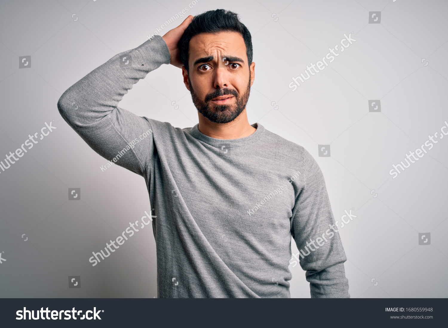 Young handsome man with beard wearing casual sweater standing over white background confuse and wonder about question. Uncertain with doubt, thinking with hand on head. Pensive concept. #1680559948