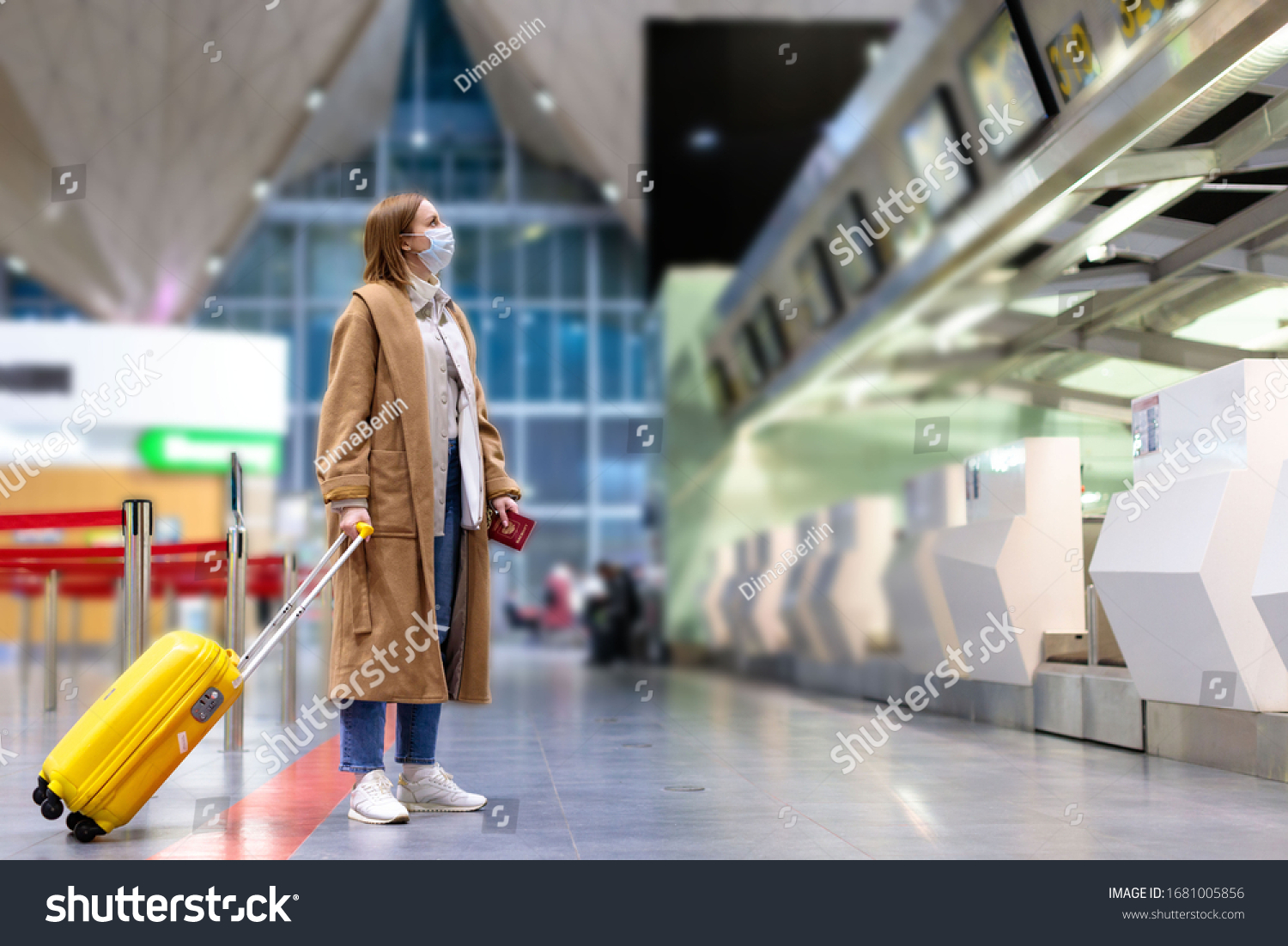 Woman with luggage stands at almost empty check-in counters at the airport terminal due to coronavirus pandemicCovid-19 outbreak travel restrictions. Flight cancellation.Quarantine all over the world #1681005856